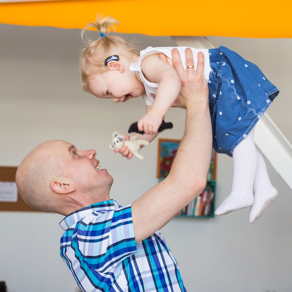 network hearing parent lifting happy child wearing hearing aids